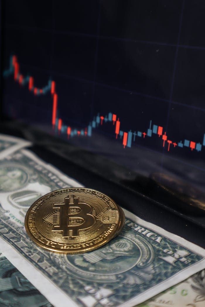 digital Bitcoin coin resting on a dollar bill with a stock market chart on a screen behind, symbolizing cryptocurrency investment.